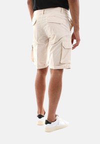Pantaloni cargo beige con due tasche laterali e una tasca posteriore, realizzati in materiale leggero, presentano una vestibilità comoda e orli rifiniti.