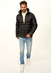 Black puffer jacket with a chevron design, zip closure, and adjustable hood, paired with light blue jeans and white sneakers.