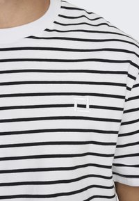 Stribet bomulds T-shirt i sort og hvid med rund halsudskæring og et broderet logo på venstre bryst. Blød tekstur, klassisk pasform.