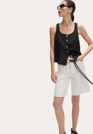 Top in lino nero con bottoni frontali, abbinato a pantaloncini in denim bianchi con orli sfilacciati e una cintura nera, su uno sfondo neutro.