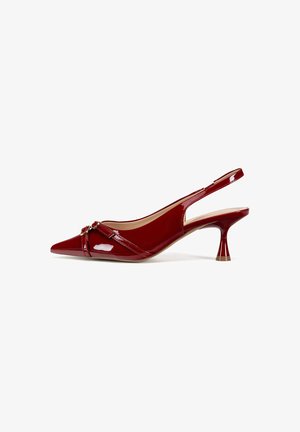 Piros lakkbőr szandál, hegyes orral és formázott sarokkal. Keresztbe tett pánttal rendelkezik, amelyen egy kis díszítés található.