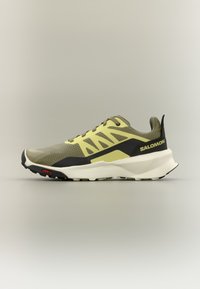 Αθλητικό παπούτσι Salomon σε ελιά πράσινο και κίτρινο με μαύρες λεπτομέρειες και λευκή παχιά σόλα, εμφανίζεται από το πλάι σε απλό φόντο.