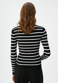 Mustavalkoinen raidallinen ribbipaita pitkillä hihoilla ja istuvalla muotoilulla, jossa on pyöreä pääntie ja hienovaraiset tekstuurit.