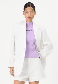 White tailored blazer over a lavender ribbed knit top with black text, paired with white denim shorts, featuring a relaxed fit and clean lines.