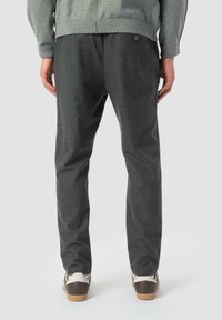 Pantalons gris foncé, fuselés, dotés d'une texture douce, de détails de boutons et d'une taille élastique, associés à des baskets de couleur claire.