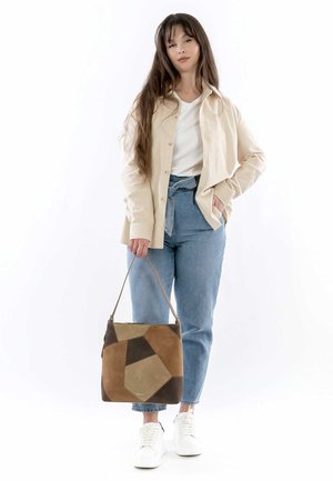 Beige button-up shirt over a white T-shirt, blue high-waisted jeans, and a multi-colored patchwork handbag. White sneakers complete the outfit.