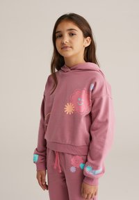 Rózsaszín kapucnis pulóver grafikás virág- és mosolygós mintákkal. Puha anyag, rövid fazon, bordázott mandzsetták, és hozzáillő melegítőnadrágok.