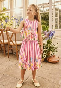 Vestido a rayas rosa y blanco con falda acampanada y top sin mangas; combinado con zapatos de color crema. Presenta estampados de flores vibrantes.