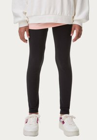Svarta leggings i ett slätt, stretchigt material i kombination med en vit oversized sweatshirt och vita sneakers med rosa detaljer.