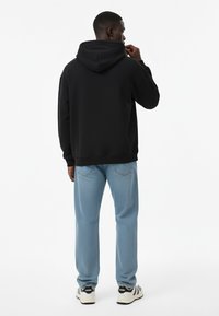 Felpa nera con cappuccio, vestibilità comoda, abbinata a jeans tessuti blu chiaro. Sneakers bianche e nere con accenti grafici sulle suole.
