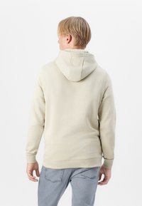 Un sweat à capuche beige en tissu doux avec une coupe décontractée, doté d'une capuche à cordon et de poignets côtelés, associé à un jean gris délavé.