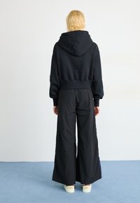 Svart kort hoodie med huva, kombinerad med luftiga svarta byxor. Slät tygkvalitet med minimala detaljer. Vita skor fulländar looken.