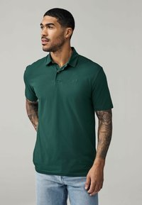 Grünes Poloshirt aus glattem Stoff, mit kurzen Ärmeln, Kragen und einer Knopfleiste mit einem einzigen Knopf. Mit einem dezenten Logo auf der Brust.