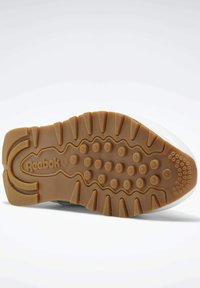 Suela de zapatilla Reebok en goma marrón con patrones circulares y acanalados; presenta características de agarre texturizado; borde superior blanco visible.