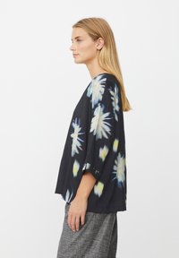 Sort top med mønster af blå og gule blomster, har løse ærmer og en afslappet pasform, kombineret med grå teksturerede bukser.