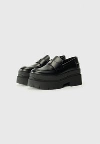 Black platform loafers with a sleek leather upper, featuring a smooth texture and a small decorative logo on the front.
