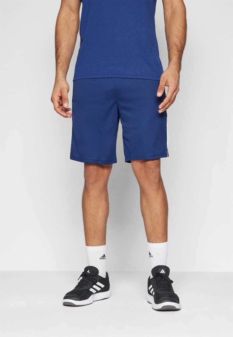 Tenue athlétique pour homme comprenant un t-shirt bleu, un short bleu avec des rayures blanches sur les côtés, des baskets noires et des chaussettes blanches.