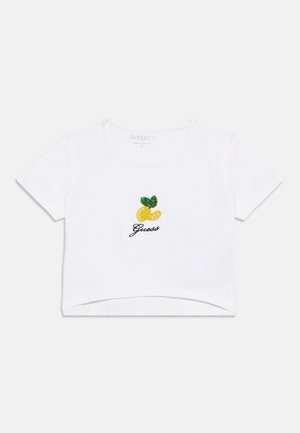 Λευκό κοντομάνικο cropped t-shirt με μικρό κεντητό κίτρινο λεμόνι και πράσινο φύλλο πάνω από τη λέξη "Guess" σε μαύρο γραφικό χαρακτήρα.