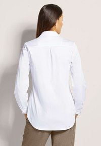 Witte long-sleeve shirt met een klassieke kraag, voorzien van een rugplooi en een gebogen zoom. Glad stof met knoopmanchetten.