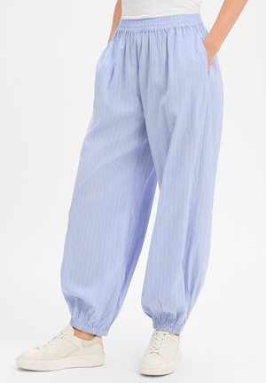 Lockere hellblaue Hose mit dünnen weißen vertikalen Streifen, elastischem Bund und Bündchen, getragen mit weißen Sneakern und einem in die Hose gesteckten weißen Oberteil.