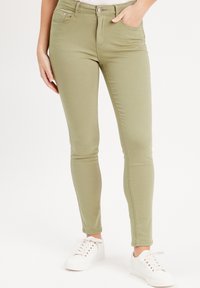 Jean skinny kaki en mélange coton extensible. Comprend des poches avant et une fermeture à bouton. Associé à des baskets blanches.