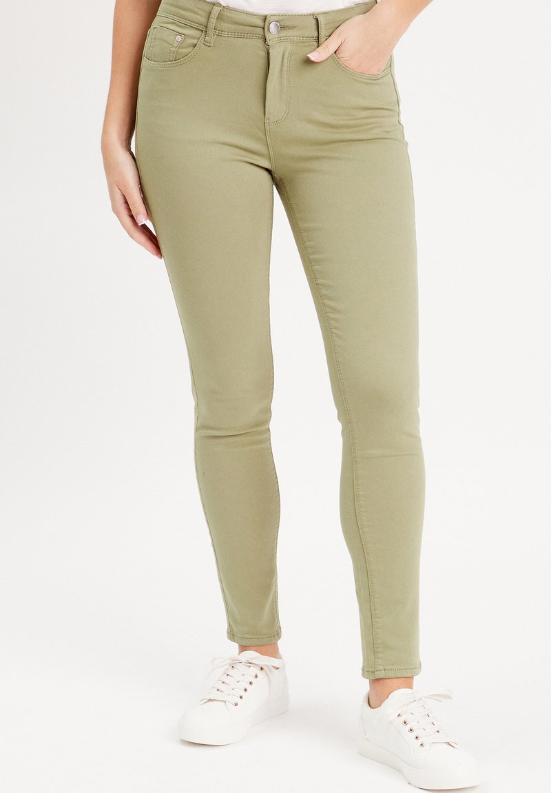 Jean skinny kaki en mélange coton extensible. Comprend des poches avant et une fermeture à bouton. Associé à des baskets blanches.