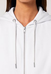 Felpa bianca con zip e cappuccio regolabile, dotata di zip argentata. Presenta una texture di tessuto morbido e un design minimalista.