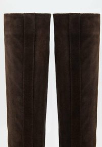 Botas de ante marrón hasta la rodilla con una textura suave y detalles de costura vertical en los lados exteriores. Construcción resistente y forma ajustada.