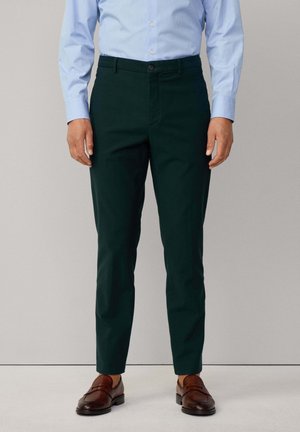Mörkgröna dressbyxor med en slät textur, smal passform och knappstängning. Bärs med en ljusblå skjorta med knappar och bruna loafers.