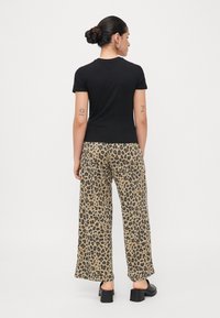 Zwarte aansluitende t-shirt gecombineerd met losse, wijdvallende broek met luipaardprint in beige en bruin. Kenmerkt zich door platte zwarte schoenen en een achteraanzicht.