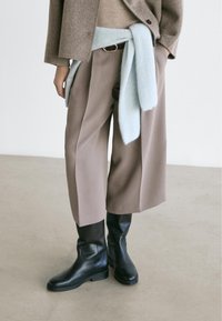 Beige wide-leg trousers with a high waist, paired with black knee-high boots. A light blue sweater tied around the waist adds texture.