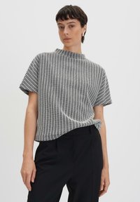 Top con maniche corte a motivi bianco e nero con scollo alto, caratterizzato da un tessuto testurizzato e una vestibilità comoda, abbinato a pantaloni neri.