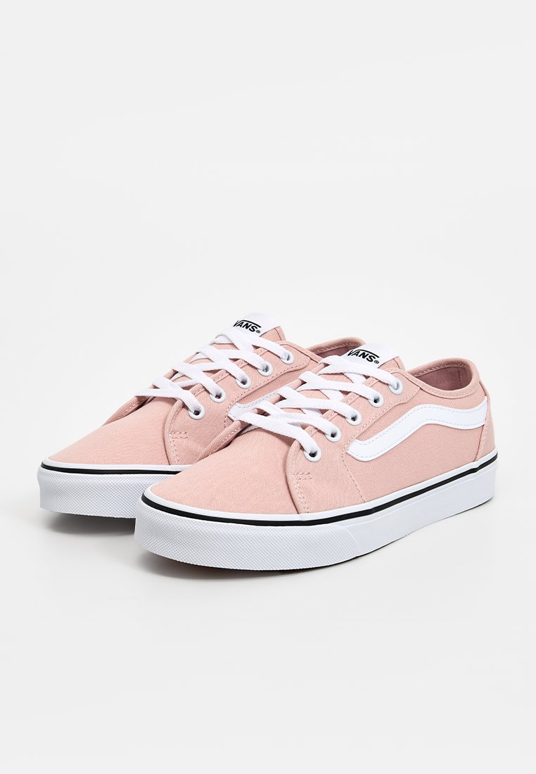 Zapatillas de lona rosa claro con cordones blancos y una franja lateral blanca. Presentan una suela de goma negra y acentos de costura.