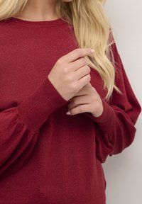 Pull en maille bordeaux avec des poignets côtelés et une finition douce et texturée. Doté de manches froncées et d'un col rond.