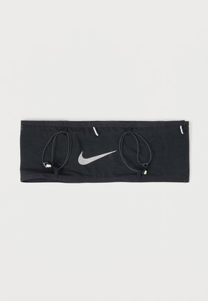 Brazalete deportivo rectangular negro con lazos elásticos ajustables y un logo blanco de Nike en forma de swoosh centrado en la parte frontal.