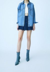 Riflová bunda v světle modré barvě se dv�ěma předními kapsami, kombinovaná s tmavou riflovou minisukní a šedými kotníkovými botami. Hladká textura látky.