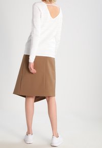 Lightweight white textured sweater with a back cutout, paired with a knee-length brown faux leather skirt and white sneakers.