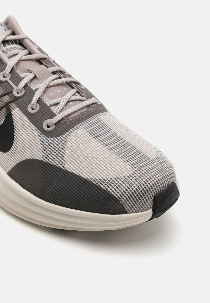 Leichter Laufschuh mit einem Obermaterial aus Mesh in Grau und Schwarz, das ein strukturiertes Gittermuster aufweist, sowie eine dicke Sohle und kontrastierende Akzente.