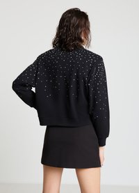 Sweat-shirt court noir avec un motif clouté dans le dos, manches longues et ourlet côtelé. Tissu lisse et coupe décontractée.