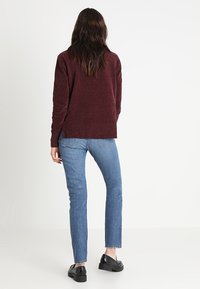 Jersey de punto burdeos con un ajuste holgado, combinado con vaqueros rectos azules. Los vaqueros tienen un dobladillo deshilachado y zapatos negros.