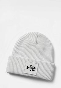 White knitted beanie hat with ribbed texture and a folded cuff, featuring a black patch of a cartoon fish skeleton design.