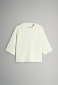 Kremna jopica iz mehkega materiala. Ima okroglo izreznico in raglan rokave do tri četrtine. Preprost, neokrašen dizajn.