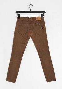 Jeans marrones ajustados con un acabado texturizado, cinco bolsillos, un parche de cuero en la cintura y un pequeño detalle en forma de corazón en el bolsillo trasero derecho.