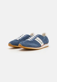 Zapatillas ligeras de ante azul con cordones blancos y adornos crema. Cuentan con una suela de goma texturizada y una forma atlética clásica.