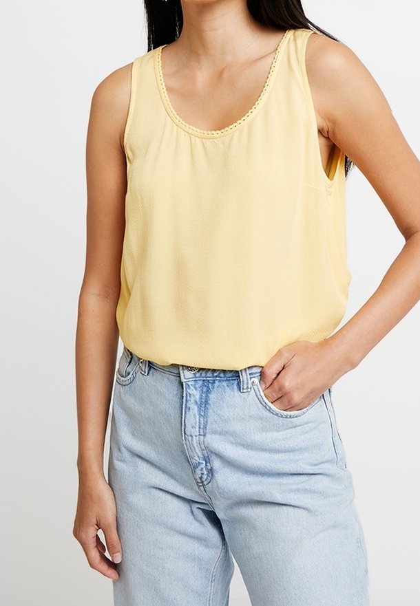 Haut sans manches jaune avec un décolleté en forme de bénitier et un tissu texturé, associé à un jean taille haute bleu clair. Comprend une poche latérale.
