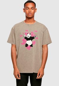 Braunes, übergroßes Baumwoll-T-Shirt mit einem schwarz-weißen Panda-Design, umgeben von rosa Herzformen. Kurze Ärmel und runder Halsausschnitt.