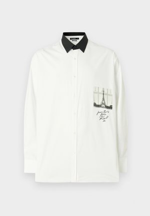 Bela srajca z dolgimi rokavi iz bombaža z črnim ovratnikom. Ima žep s sivim tiskom Eiffelovega stolpa in ročno napisanim besedilom.