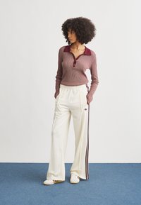 Maroon ribbed long-sleeve polo with a collar, paired with cream joggers featuring maroon stripes, and white sneakers with brown accents.