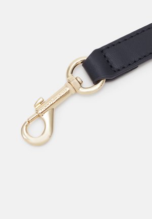 Złocony metalowy hak z grawerem "Tommy Hilfiger" przymocowany do czarnego skórzanego paska z widocznym przeszyciem.