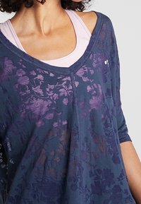 Tmavě modrý top s květinovým vzorem, volným střihem, širokým výstřihem a tříčtvrtečními rukávy. Lehká látka s jemnou texturou.